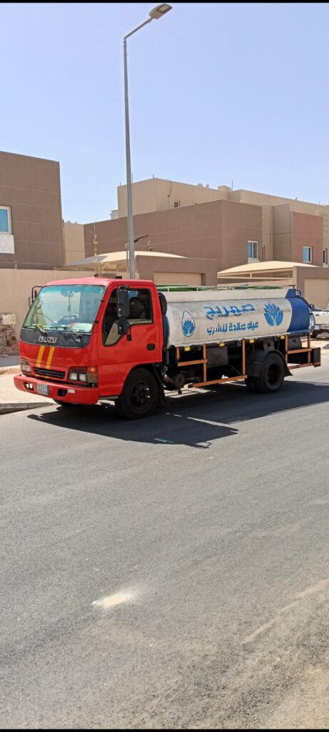 وايت مياه صالحة للشرب أحمر بخزان أبيض وأزرق متوقف في شارع سكني أمام فلل تحت سماء صافية